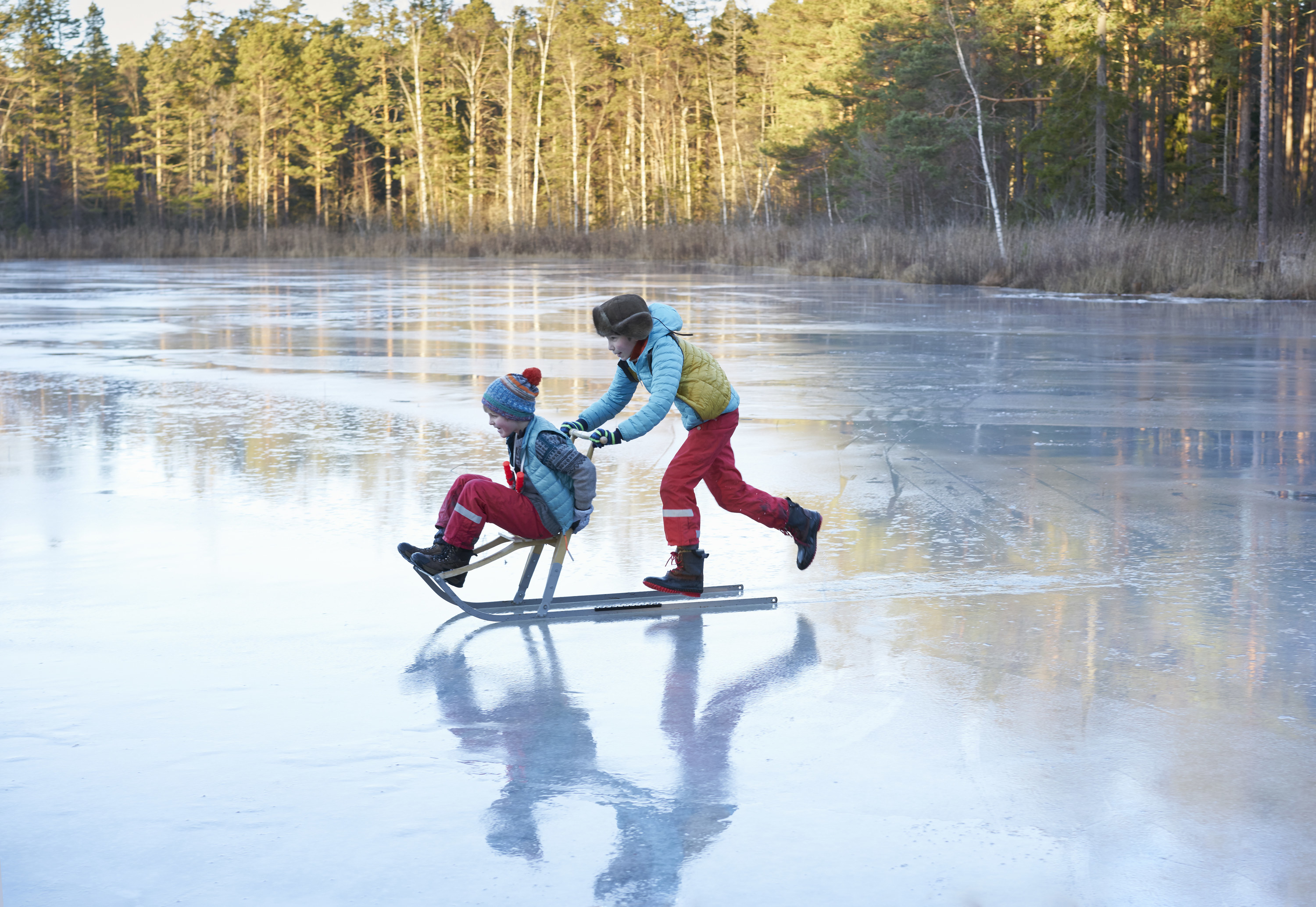 one kid pushing another on a sled/skate across a frozen water