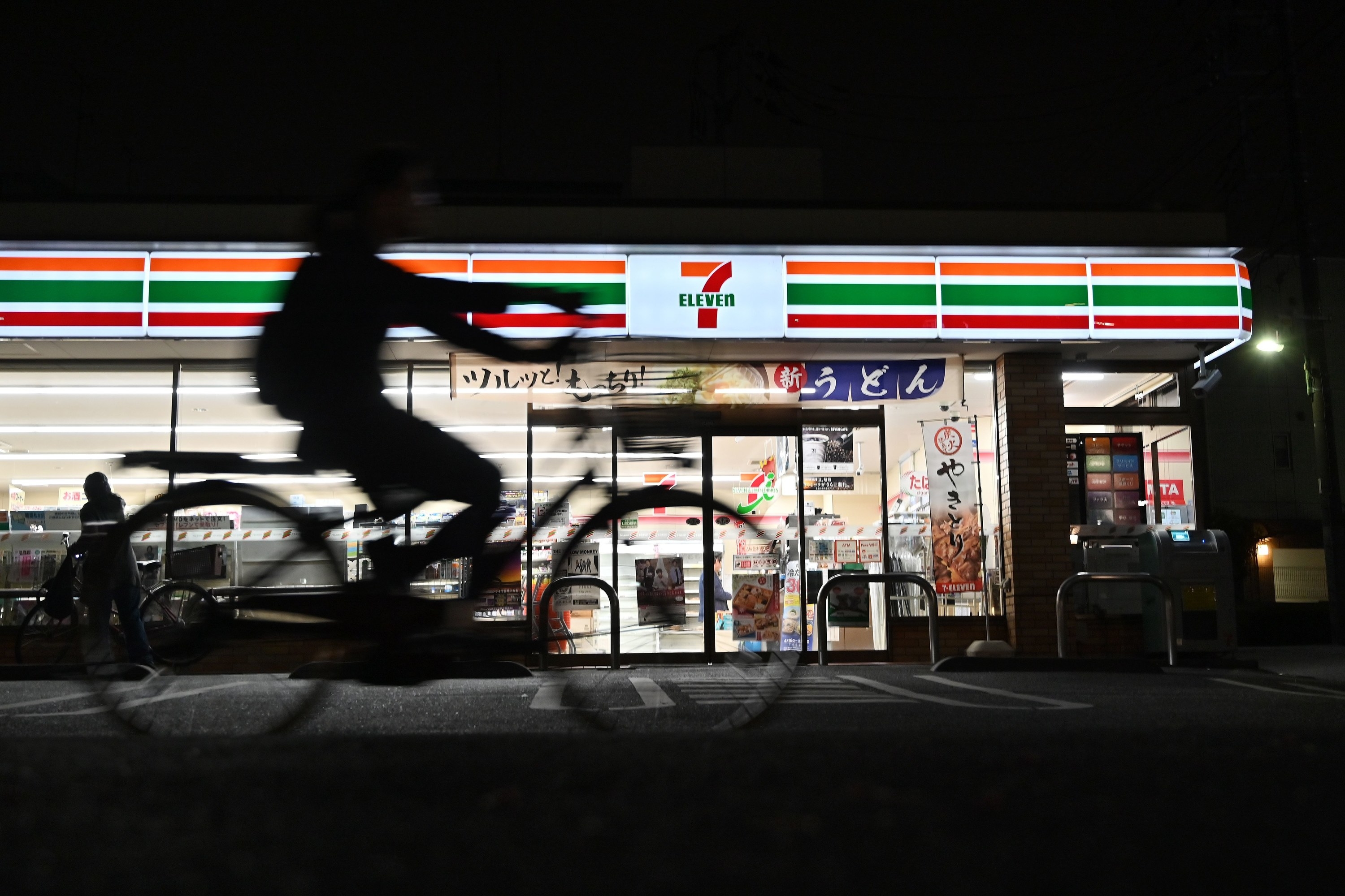 person biking in front of a 7-11 at night