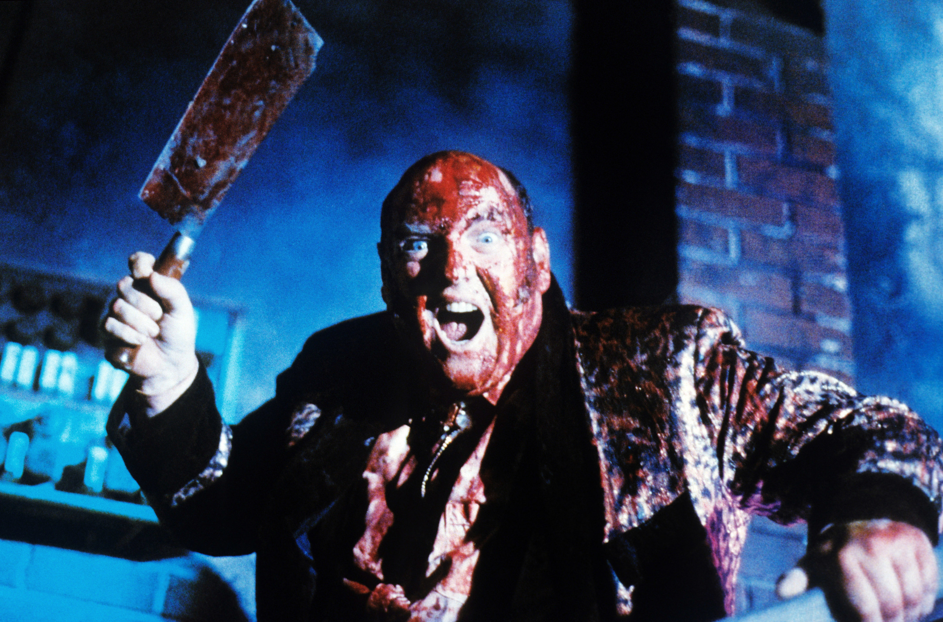 A man covered in blood holds a butcher knife