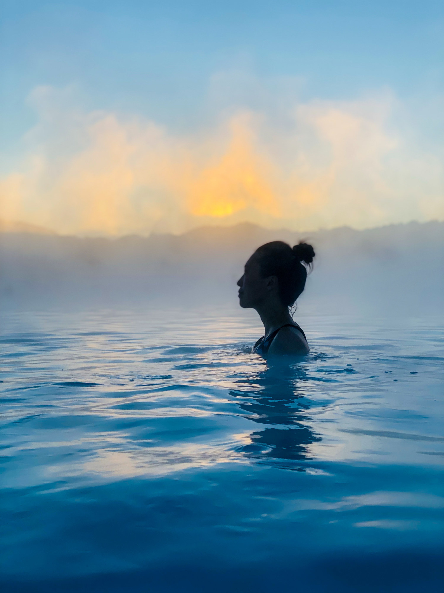 Woman bathing in Icelandic geothermal blue hot spring at sunset