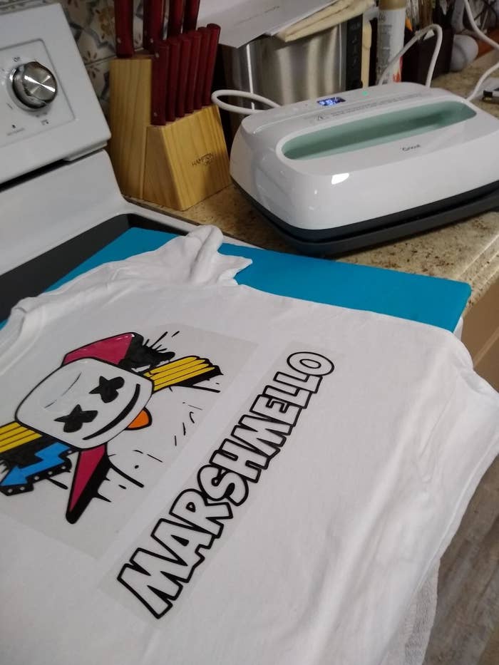 Reviewer&#x27;s photo showing t-shirt with Marshmello vinyl printed on with the Cricut heat press behind on counter