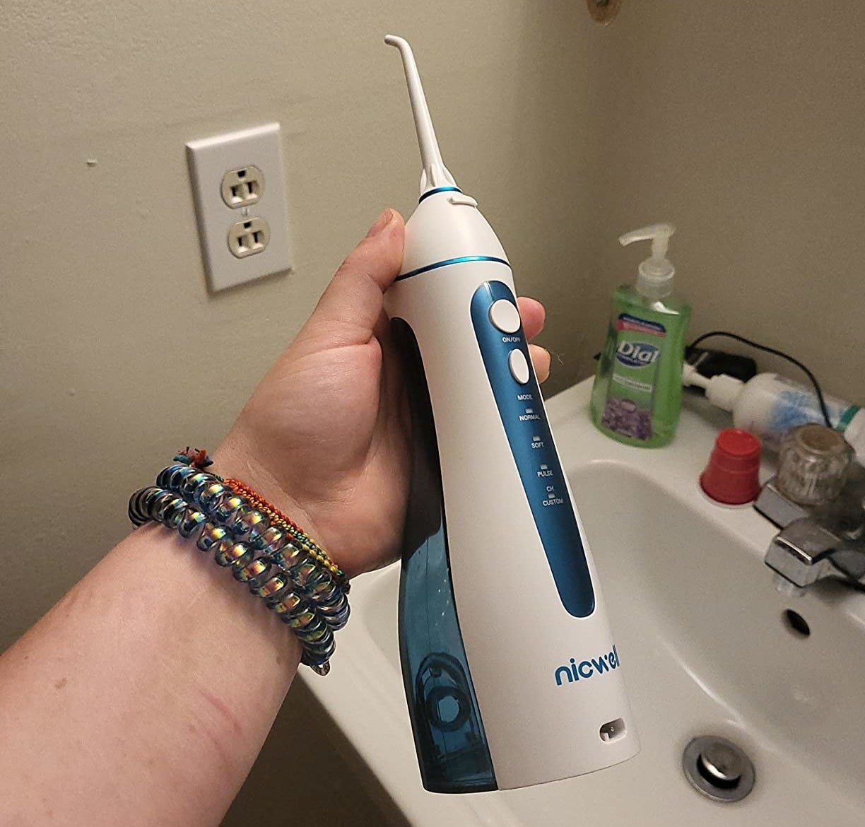 Reviewer holding the white cordless water dental flosser above bathroom sink