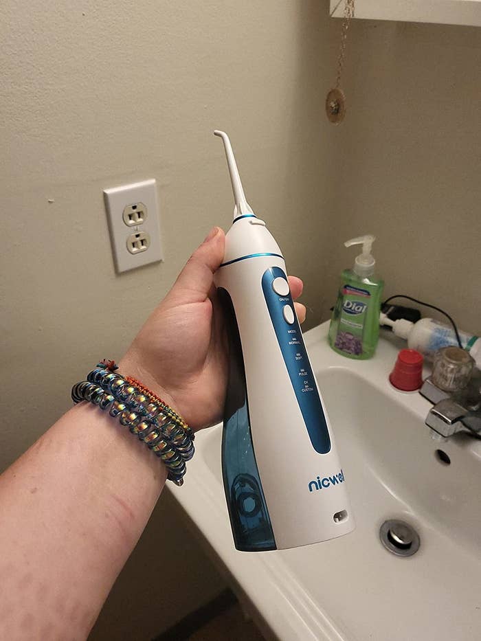 Reviewer holding the white cordless water dental flosser above bathroom sink