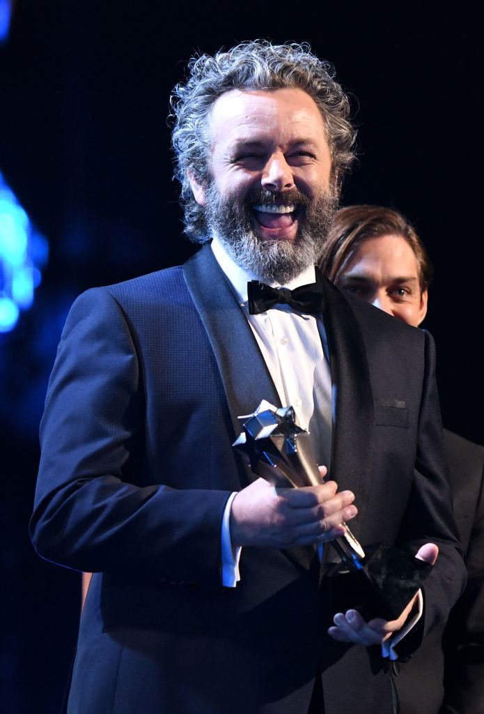 Smiling Michael in a suit and bow tie and holding an award