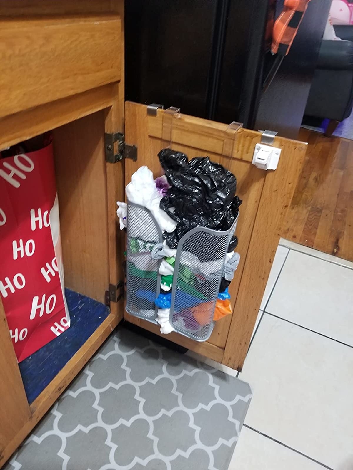 A cabinet door with a bag holder attached to the inside holding shopping bags