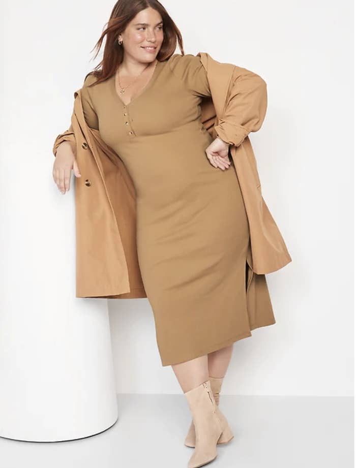 a person wearing the dress with boots and a coat while leaning against a wall