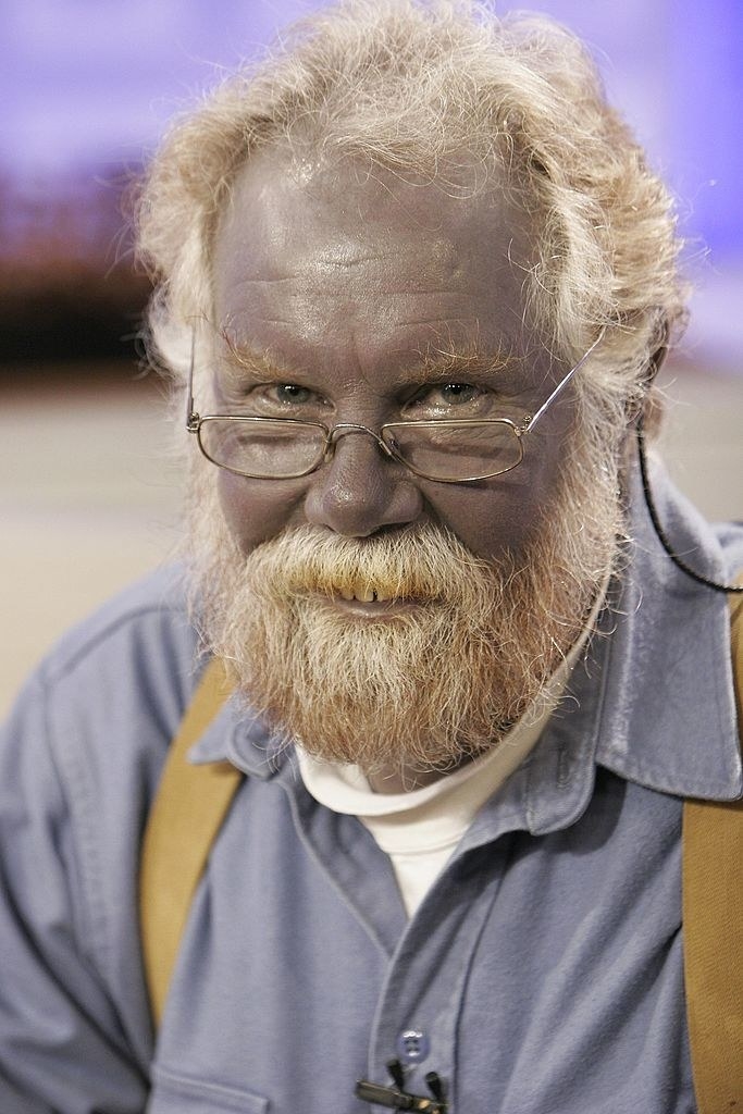 Close-up of a bespectacled man with a thick beard and mustache and bluish skin