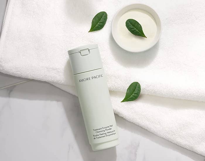 Amore Pacific Exfoliant bottle on a white towel on a marble countertop. There are green leaves laying on the counter