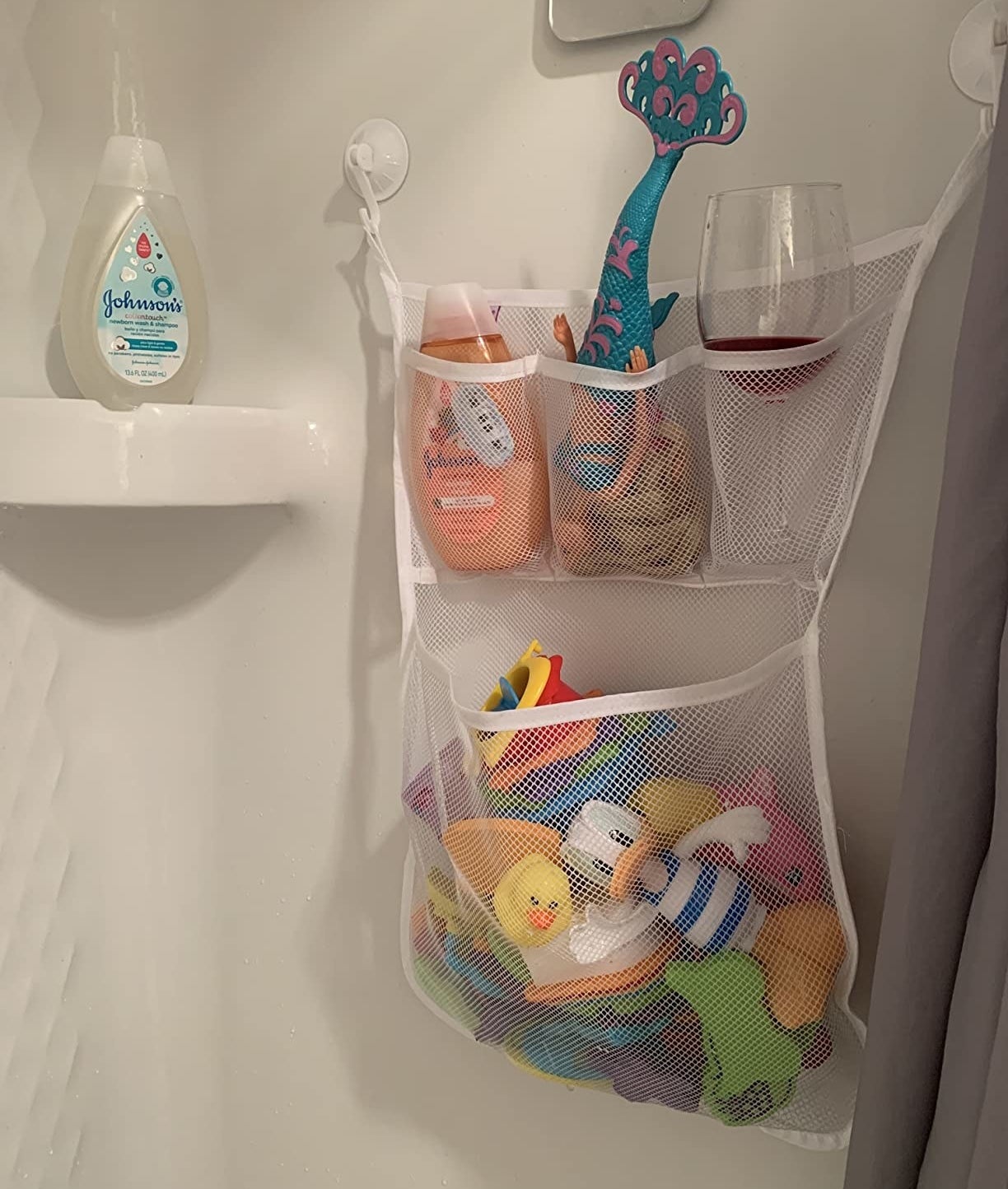 a reviewer photo of the toy organizer hanging in the shower with toys and a wine glass inside