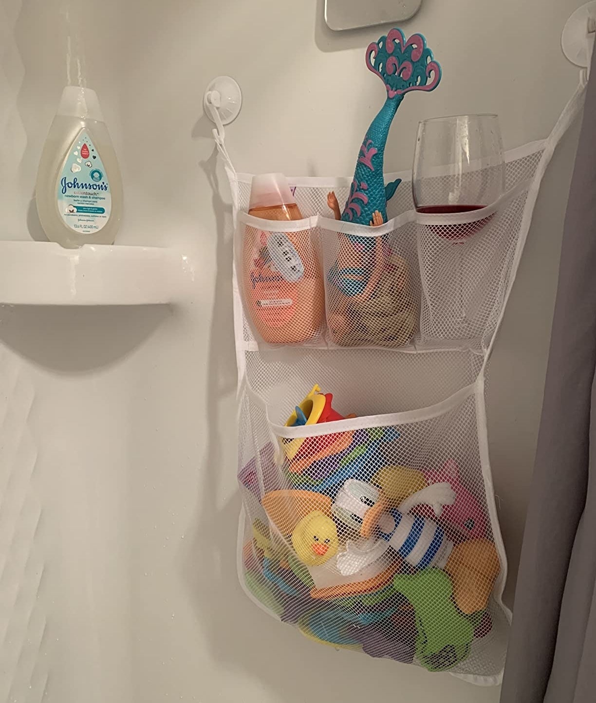 a reviewer photo of the toy organizer hanging in the shower with toys and a wine glass inside