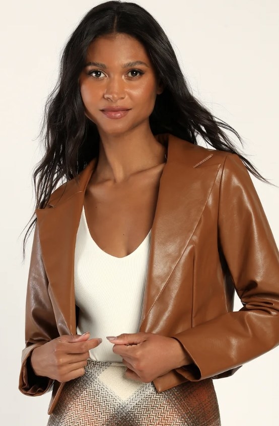 The model wears the brown jacket with a white top and brown plaid skirt