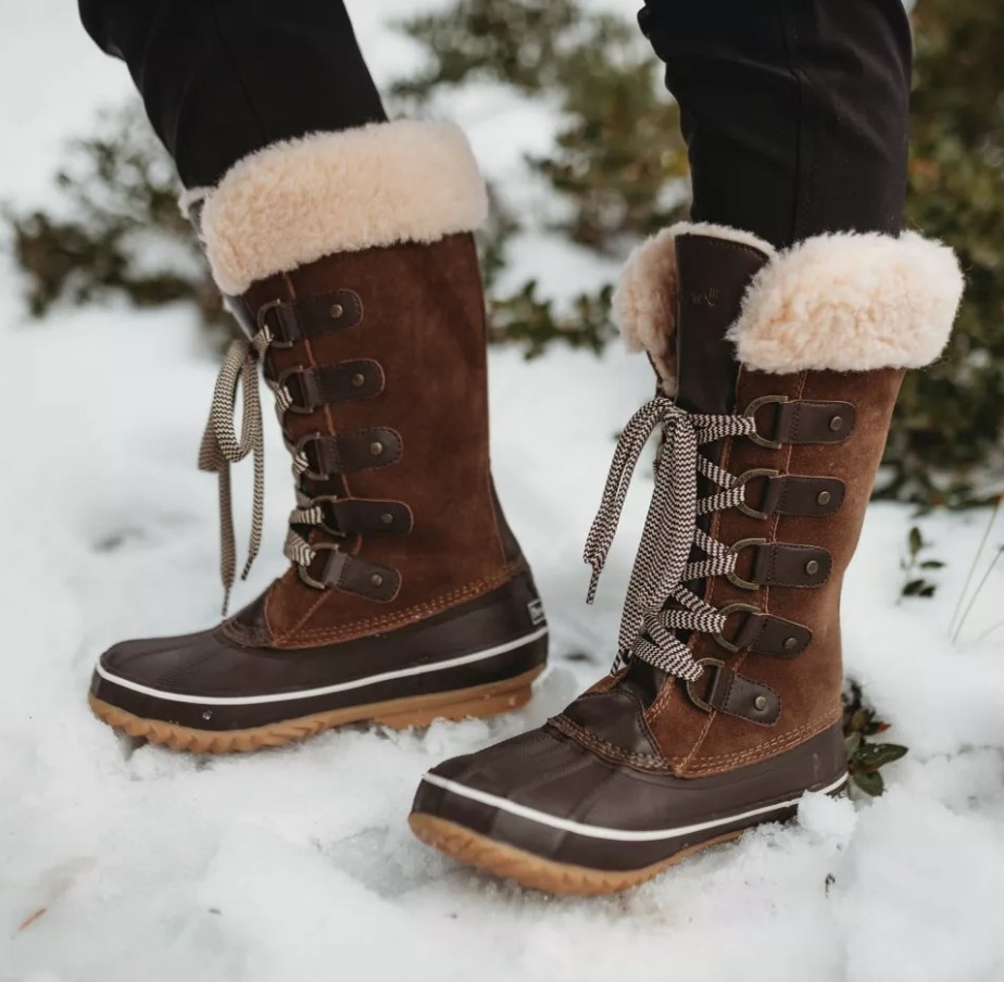 A model wearing a pair of brown, fur lined lace up winter boots