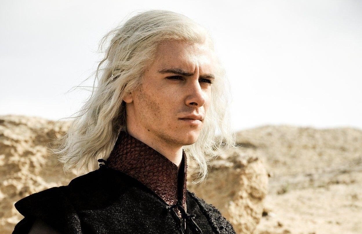 A platinum blonde haired young man stares intently within a desert landscape