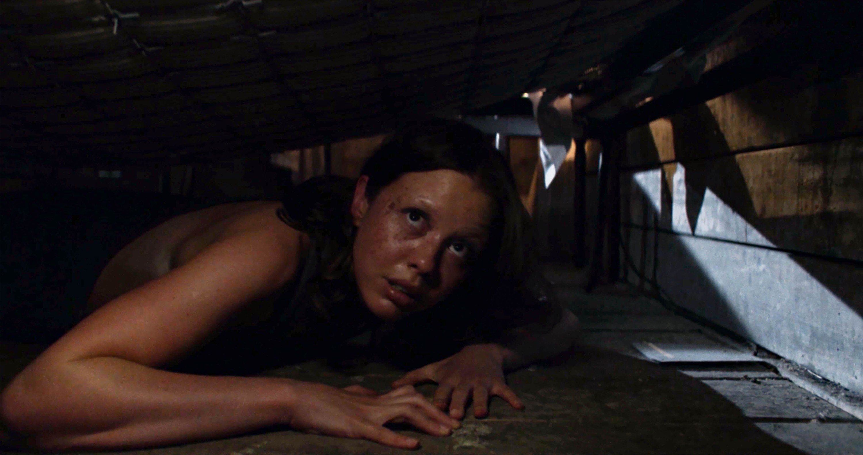 A young woman hides underneath a bed in a ramshackle cabin in “X”