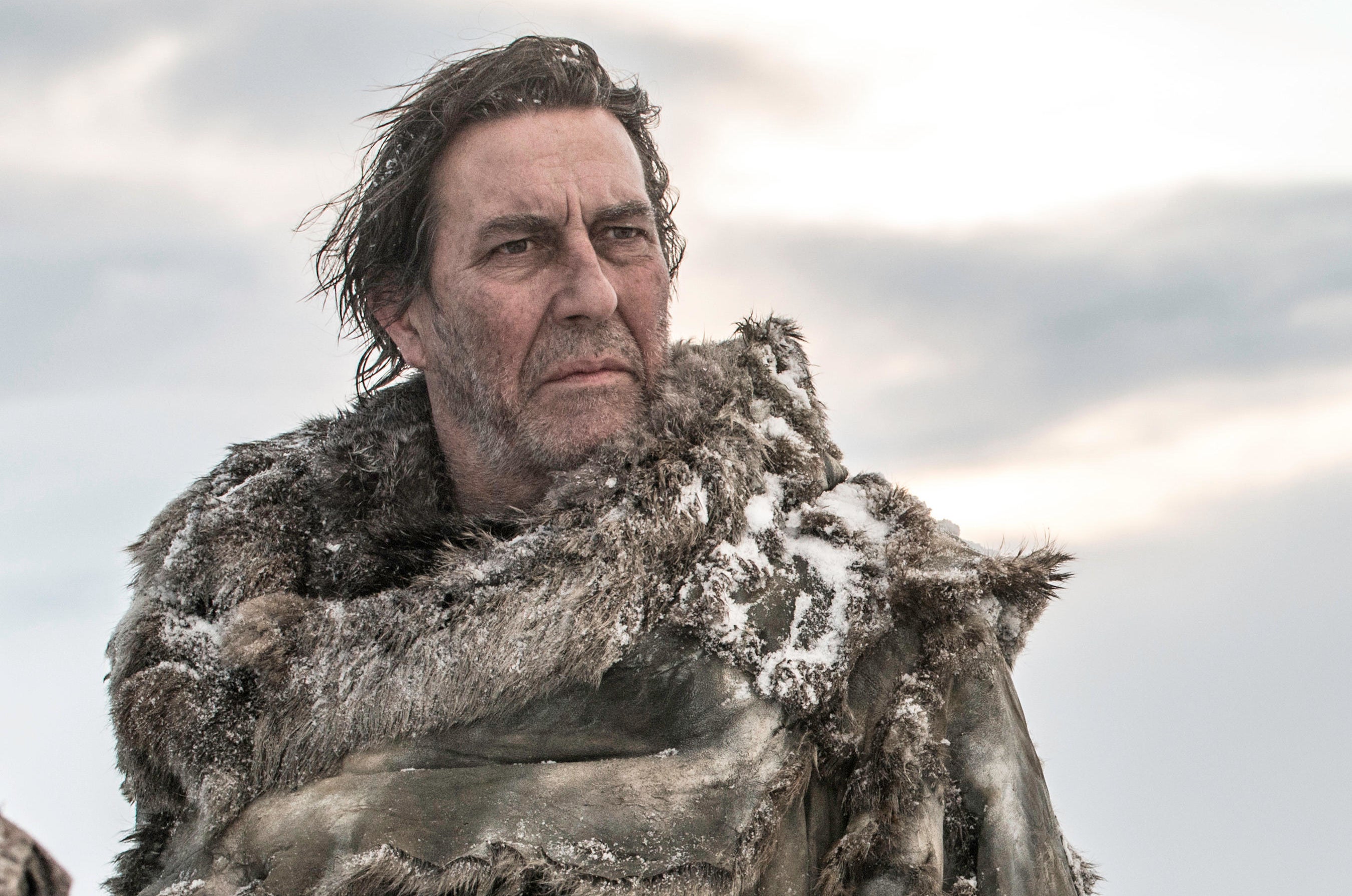 A man wearing a coat assembled from fur pelts observes a situation in a frozen tundra.