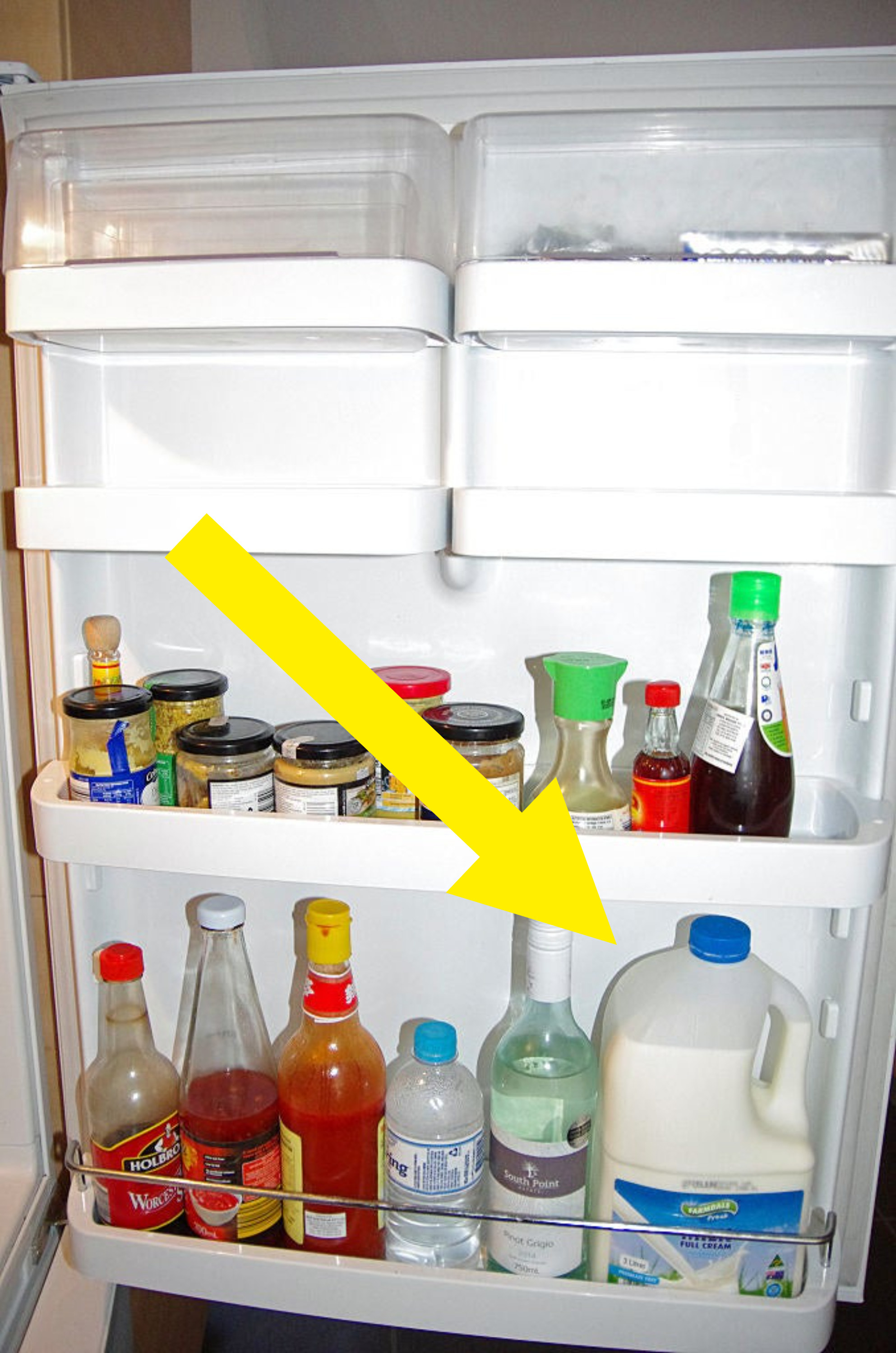 Condiments, sauces, alcohol and milk stored in the door of a home fridge.