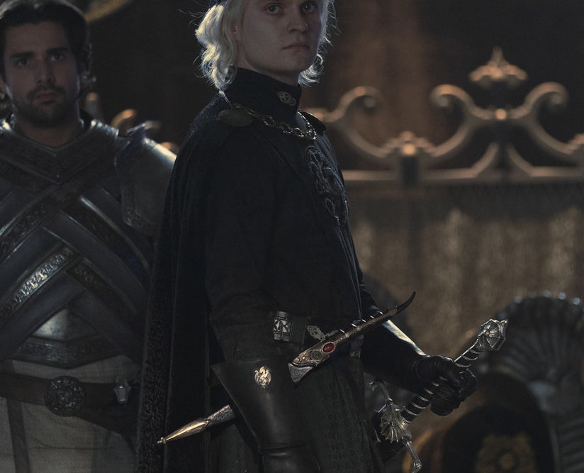 Aegon wears a crown and stands in front of Criston Cole