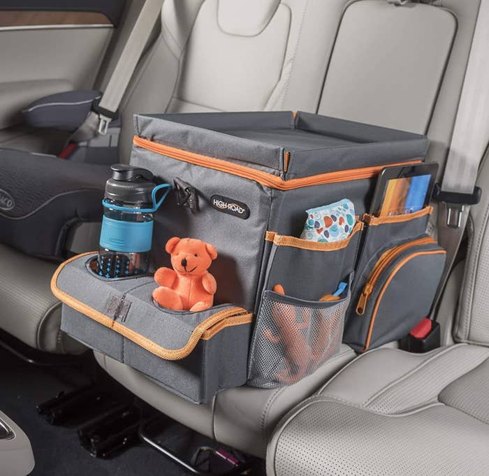 The organizer in the backseat of a car with toys, a water bottle, and a tablet in its pockets
