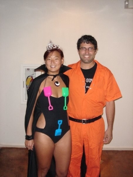 A woman in a bodysuit with spades hanging off of it and wearing a crown and cloak, hugging someone in an orange jumpsuit
