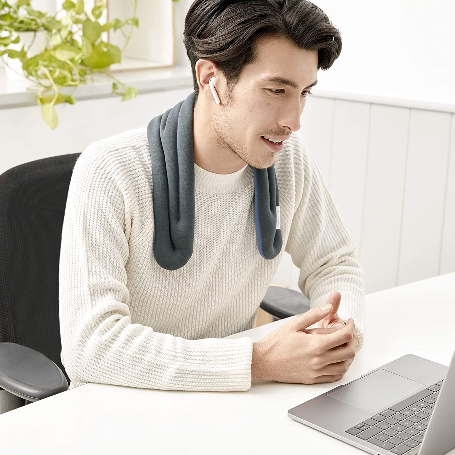 a person sitting at the computer while wearing the neck wrap