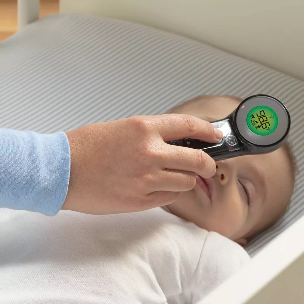 a person uses the thermometer on a sleeping baby