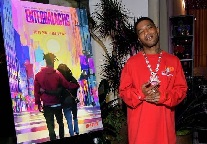 Cudi standing next to a poster for Entergalactic that says &quot;Love Will Find Us All&quot;