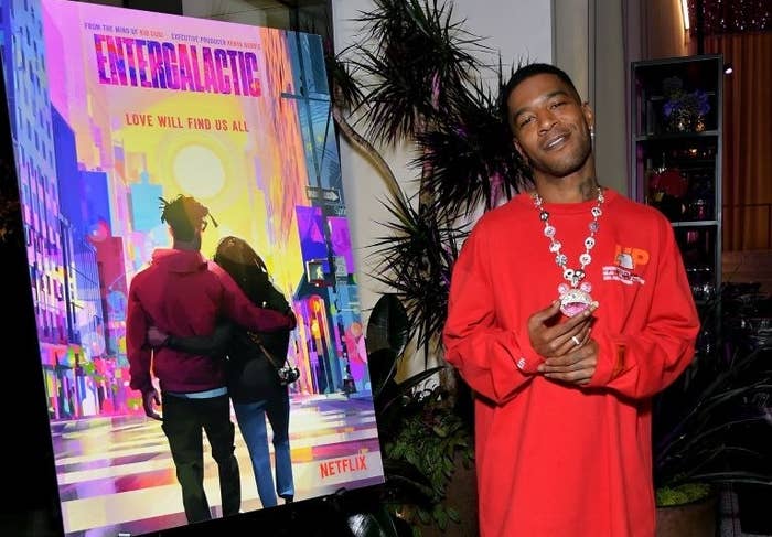 Cudi standing next to a poster for Entergalactic that says "Love Will Find Us All"
