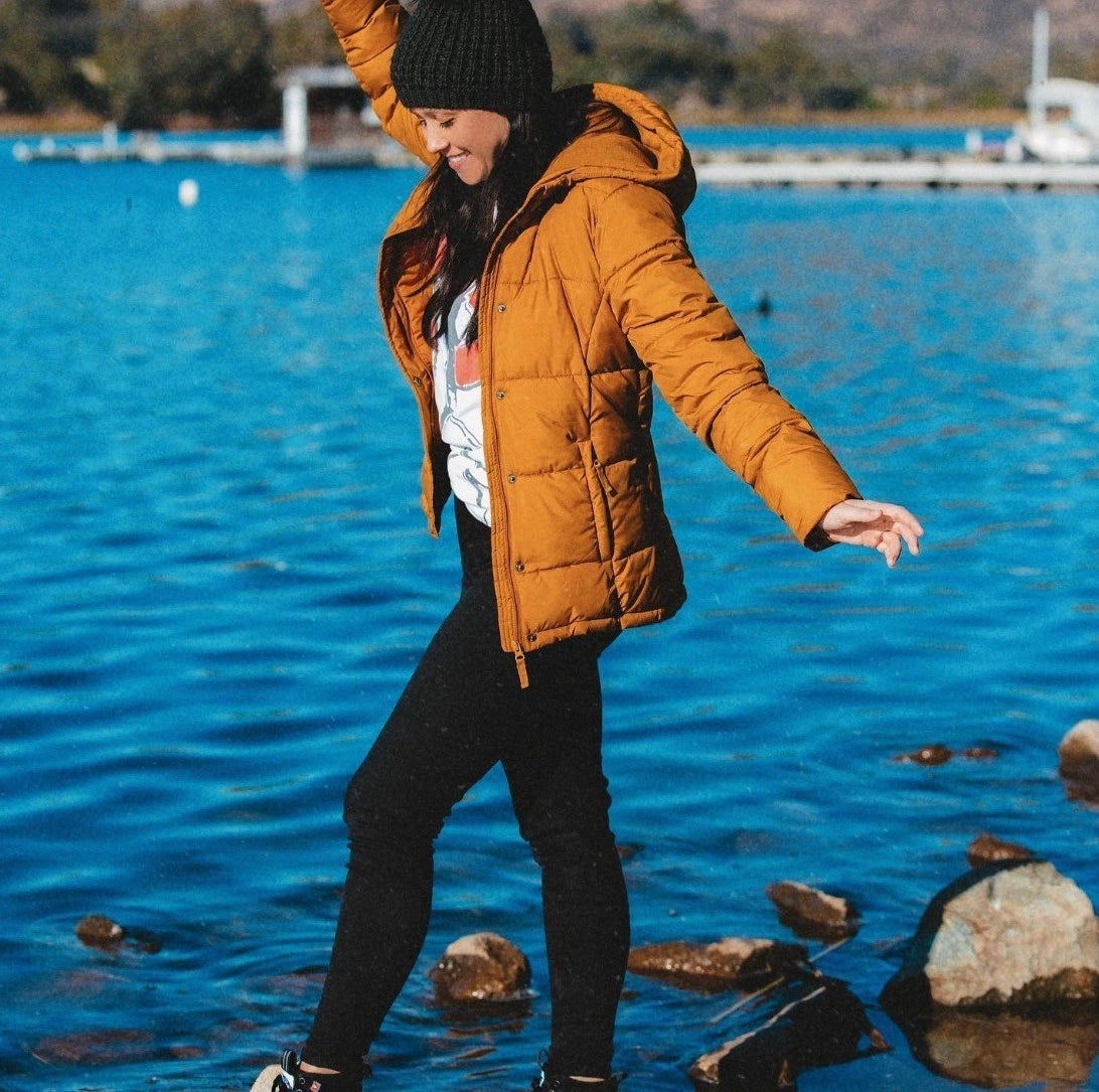 a reviewer wearing the coat in orange while next to a body of water