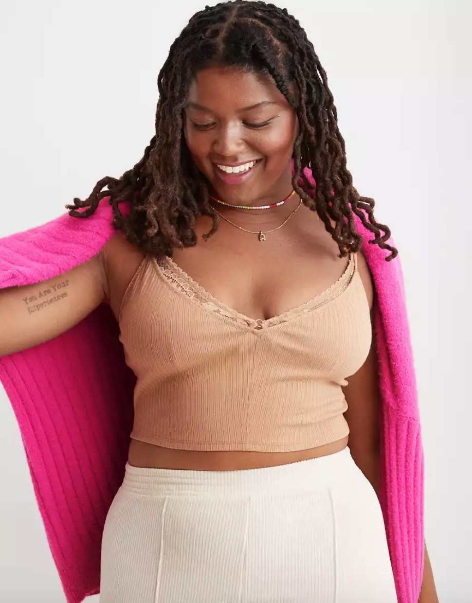 Model wearing tan colored lace bra top under pink cardigan