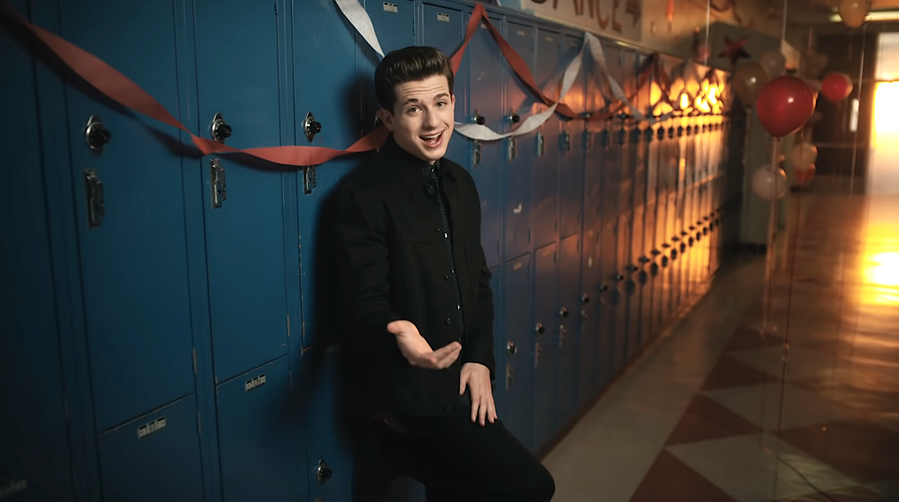 Charlie leaning against lockers in a school hallway as he sings in a music video
