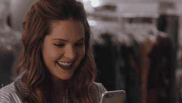 a gif of a person smiling while looking at their phone