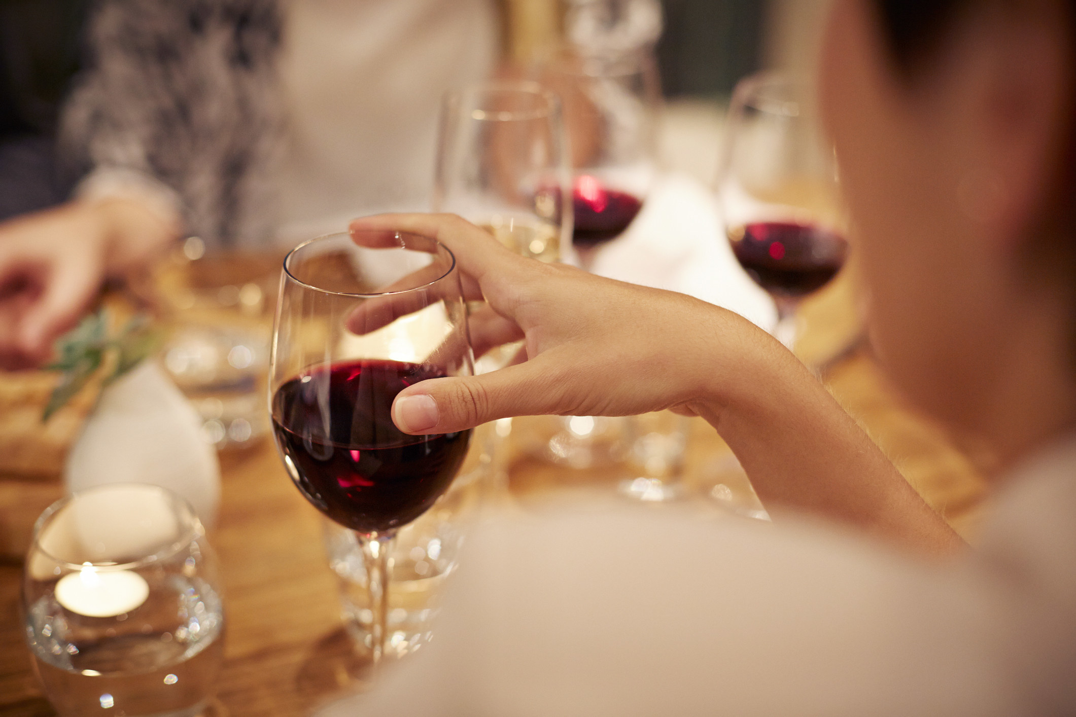 A close-up of a woman holding a glass of wine at a table.