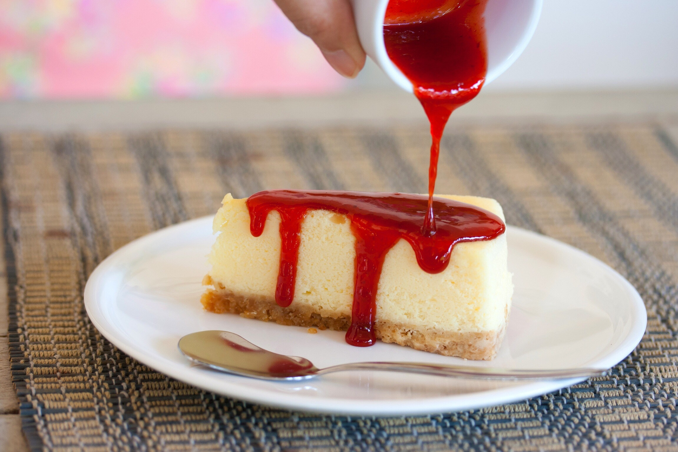 Pouring fruit syrup over a slice of cheesecake.