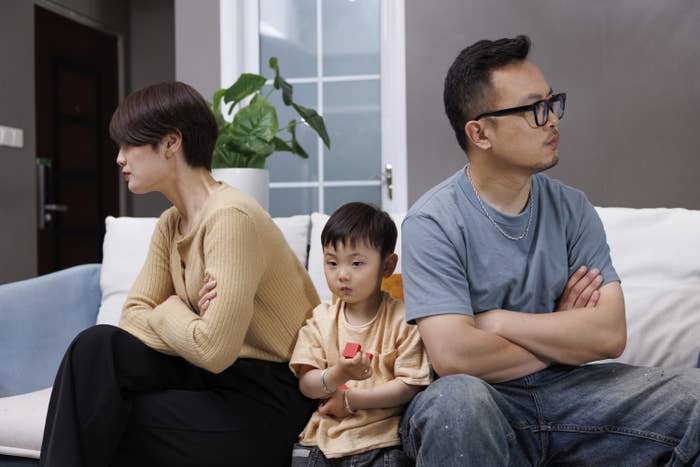 这是一个亚洲家庭。父母坐在沙发上争吵，小男孩坐在其中。他非常无助，害怕
