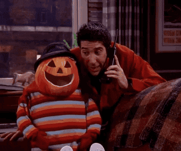 A man handing a phone to a pumpkin with a hat and sweater on