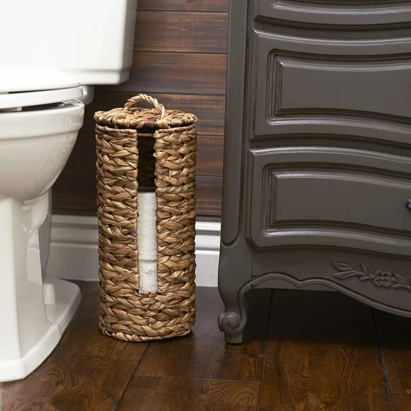 A banana leaf toilet paper holder with a wicker/rattan finish placed near a toilet
