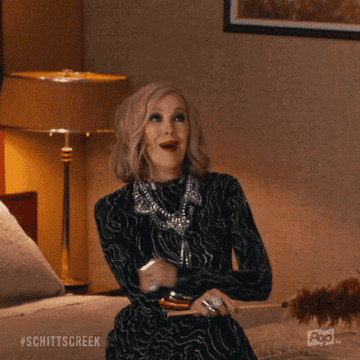 a gif of moira rose from schitts creek waving excitedly