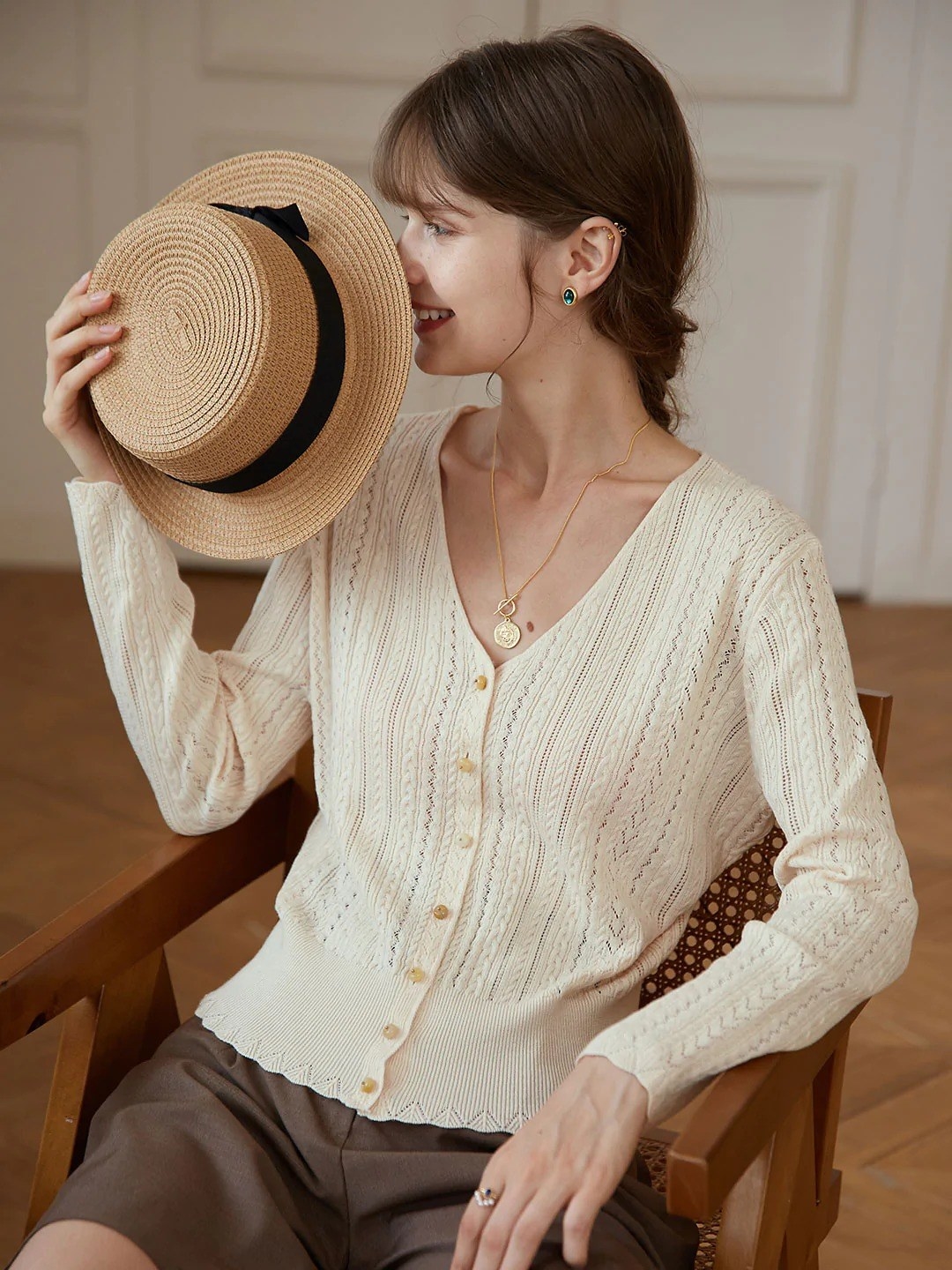 model wearing the apricot cable knit cardigan holding up a straw hat
