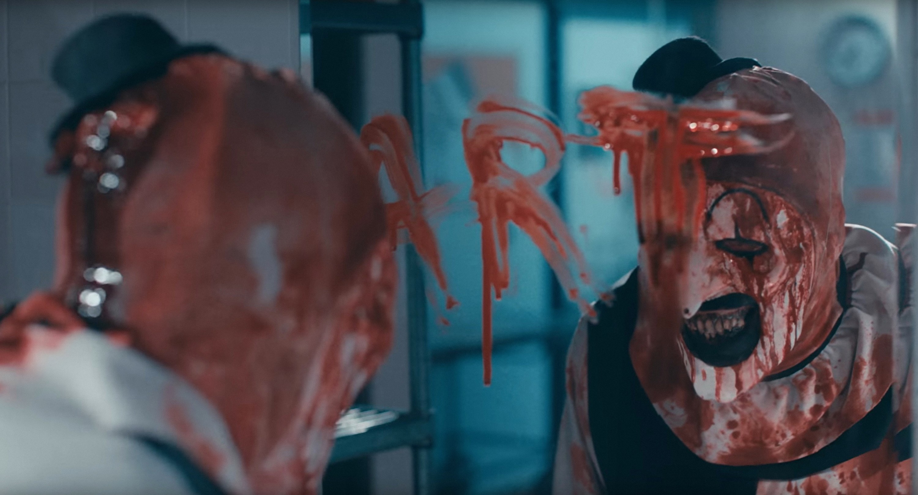 A bloodied clown standing in front of a mirror with &quot;Art&quot; written across it (in blood)
