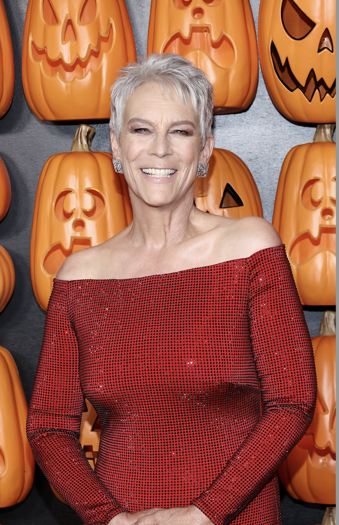 Jamie Lee Curtis smiling at an event with jack-o-lanterns behind her