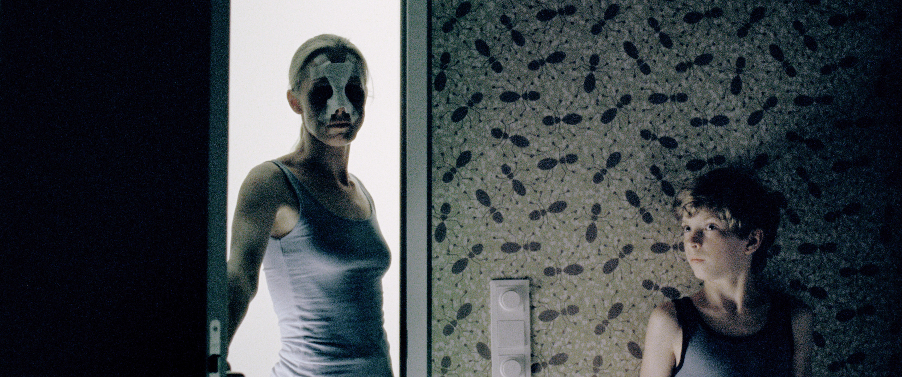 A woman in a mask enters a room while a young boy hides