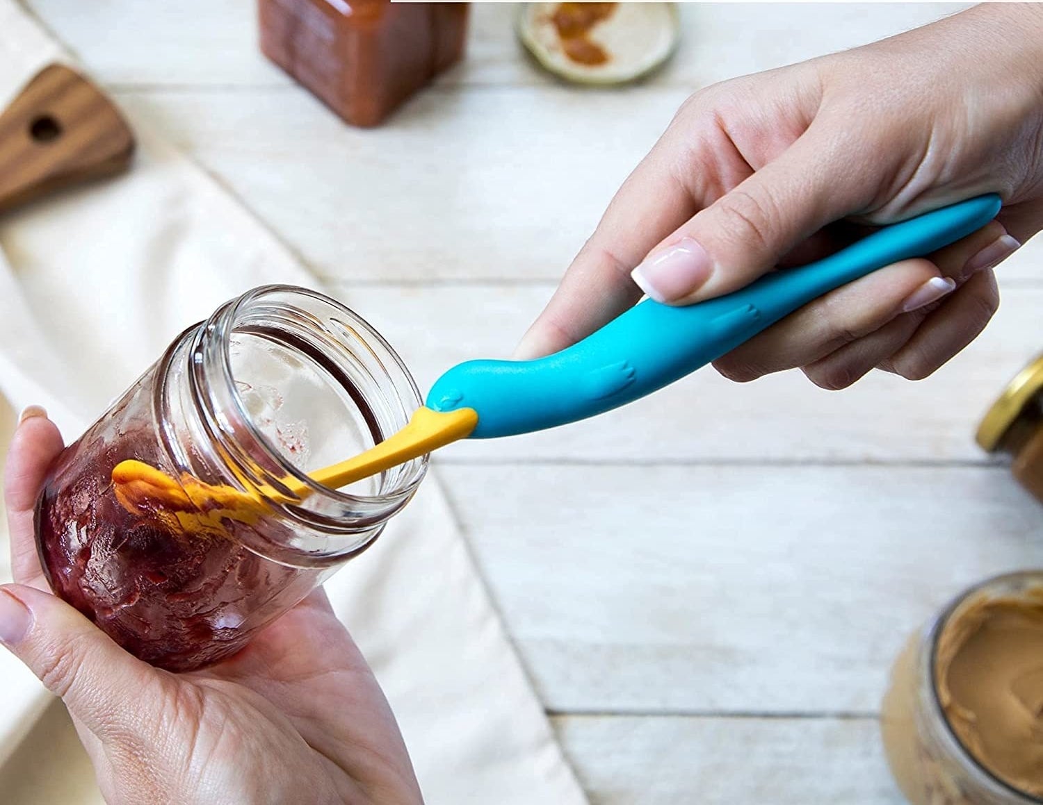 a person using the platypus shaped spatula to scoop jelly out of a jar