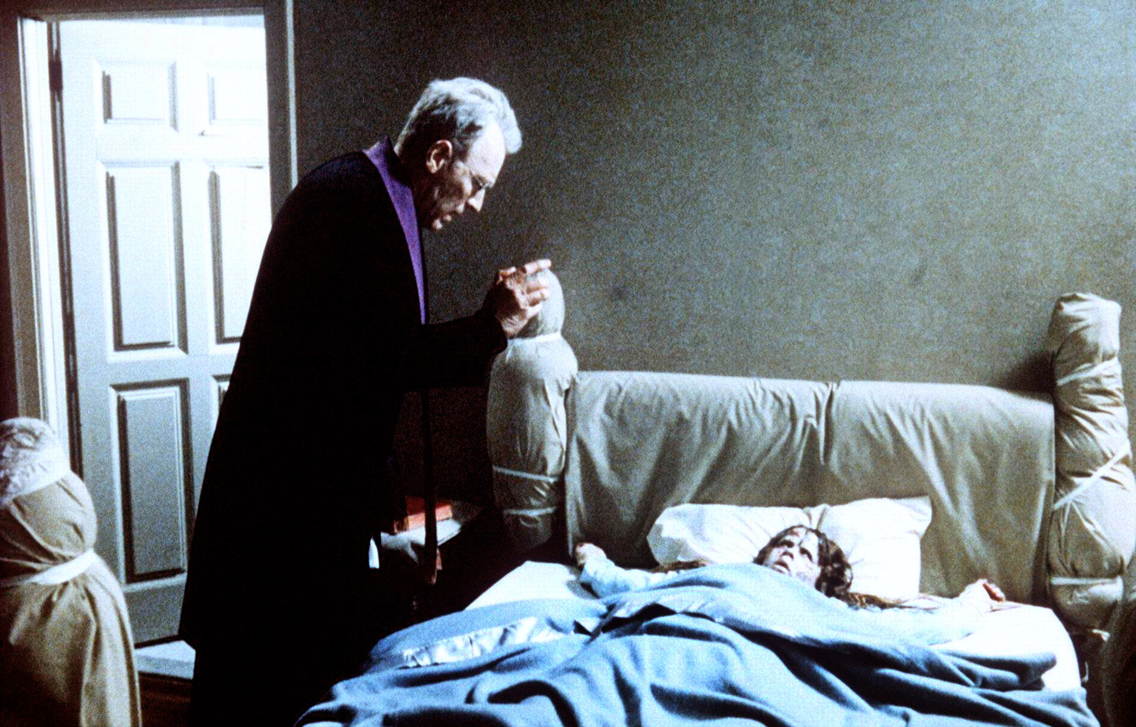 A priest stands over a young girl in bed