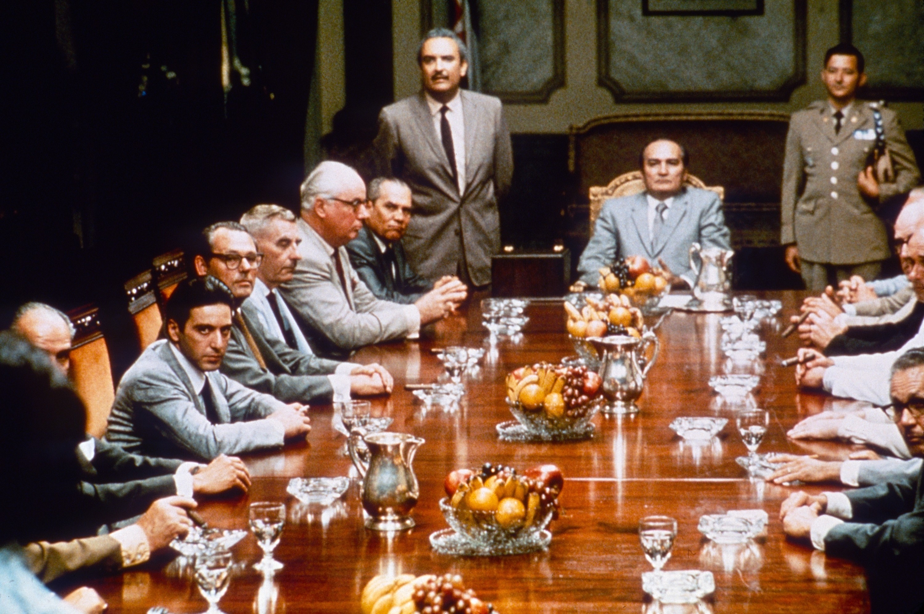 Many men in suits sitting around a large table with plates of food and glasses