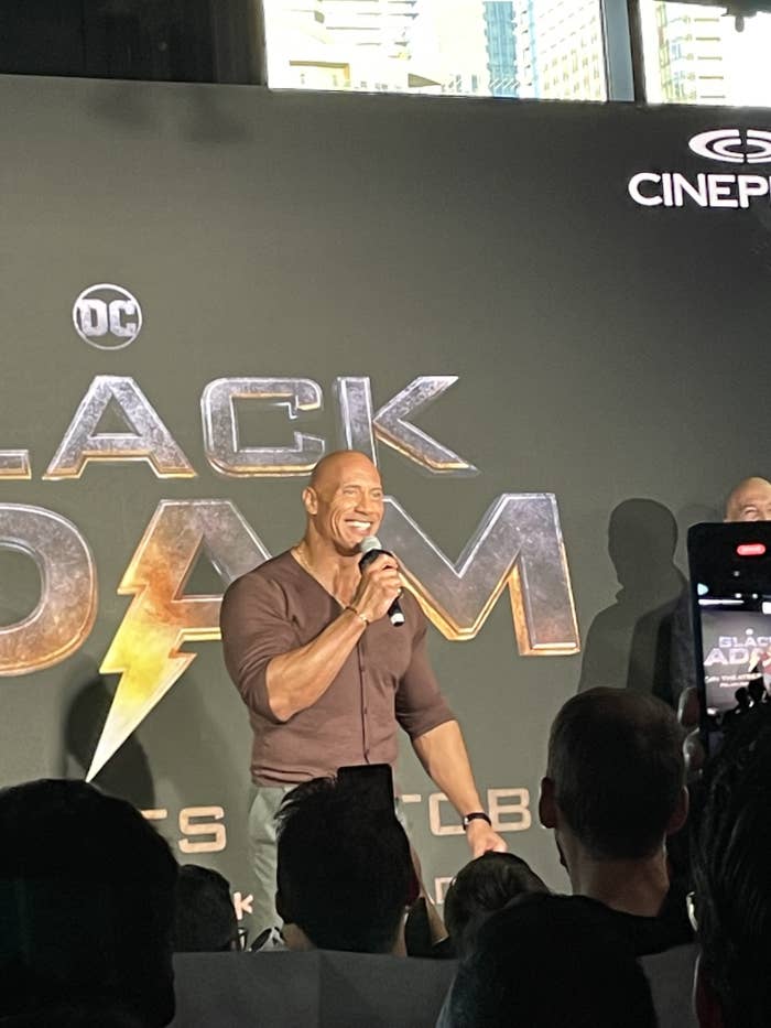 Dwayne Johnson standing in front of &quot;Black Adam&quot; backdrop