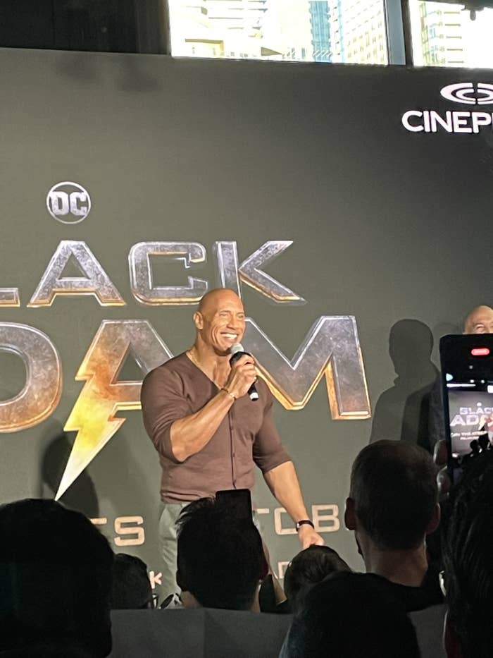Dwayne Johnson standing in front of "Black Adam" backdrop
