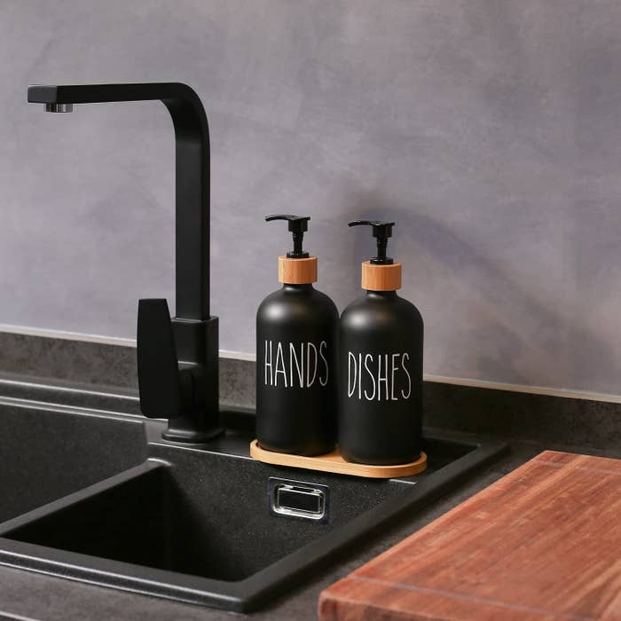A pair of minimalist soap dispensers on a sink edge and labelled hands and dishes