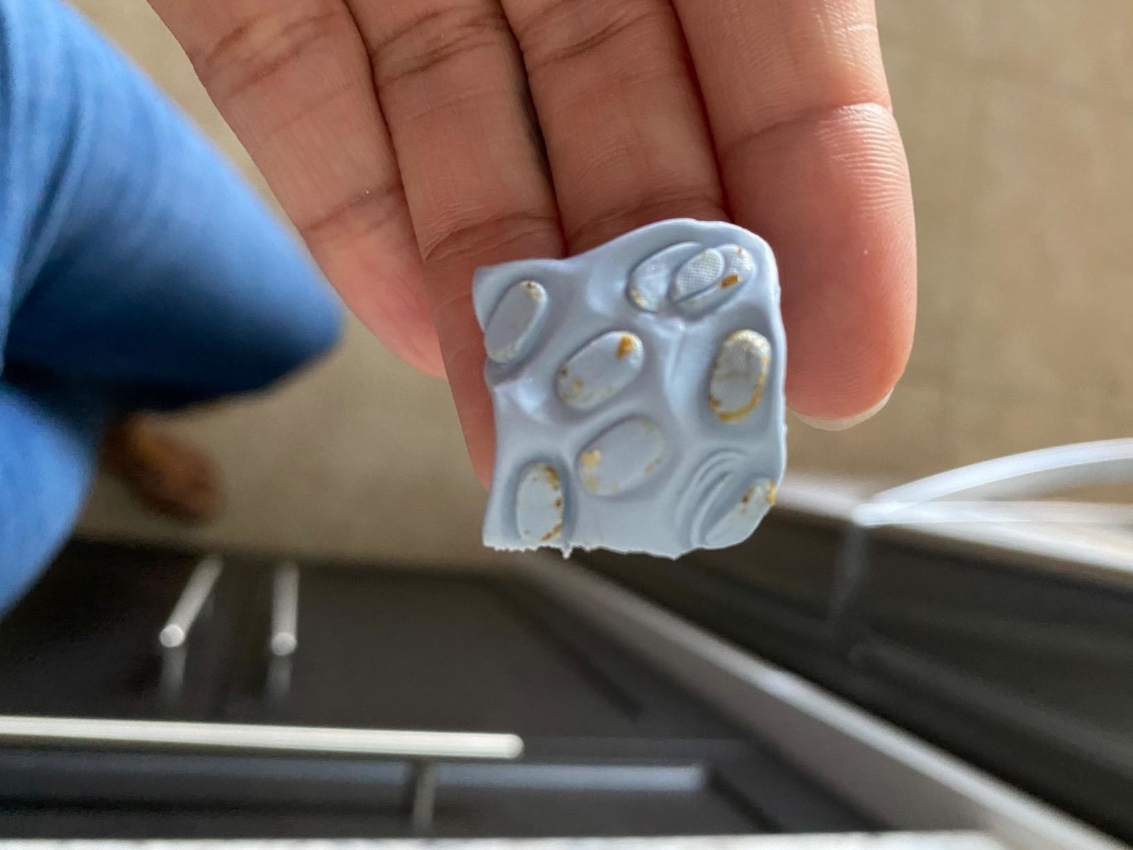 Blue square with lots of ear wax on it that was removed from a reviewer&#x27;s AirPod speaker
