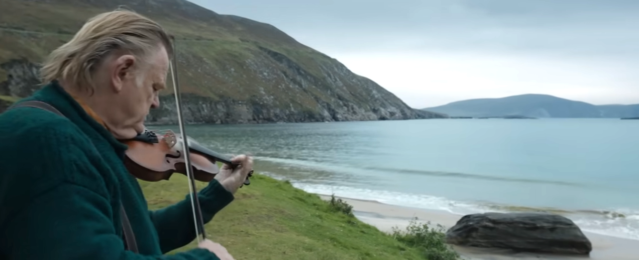 科尔姆在他家外面玩小提琴，望着海洋