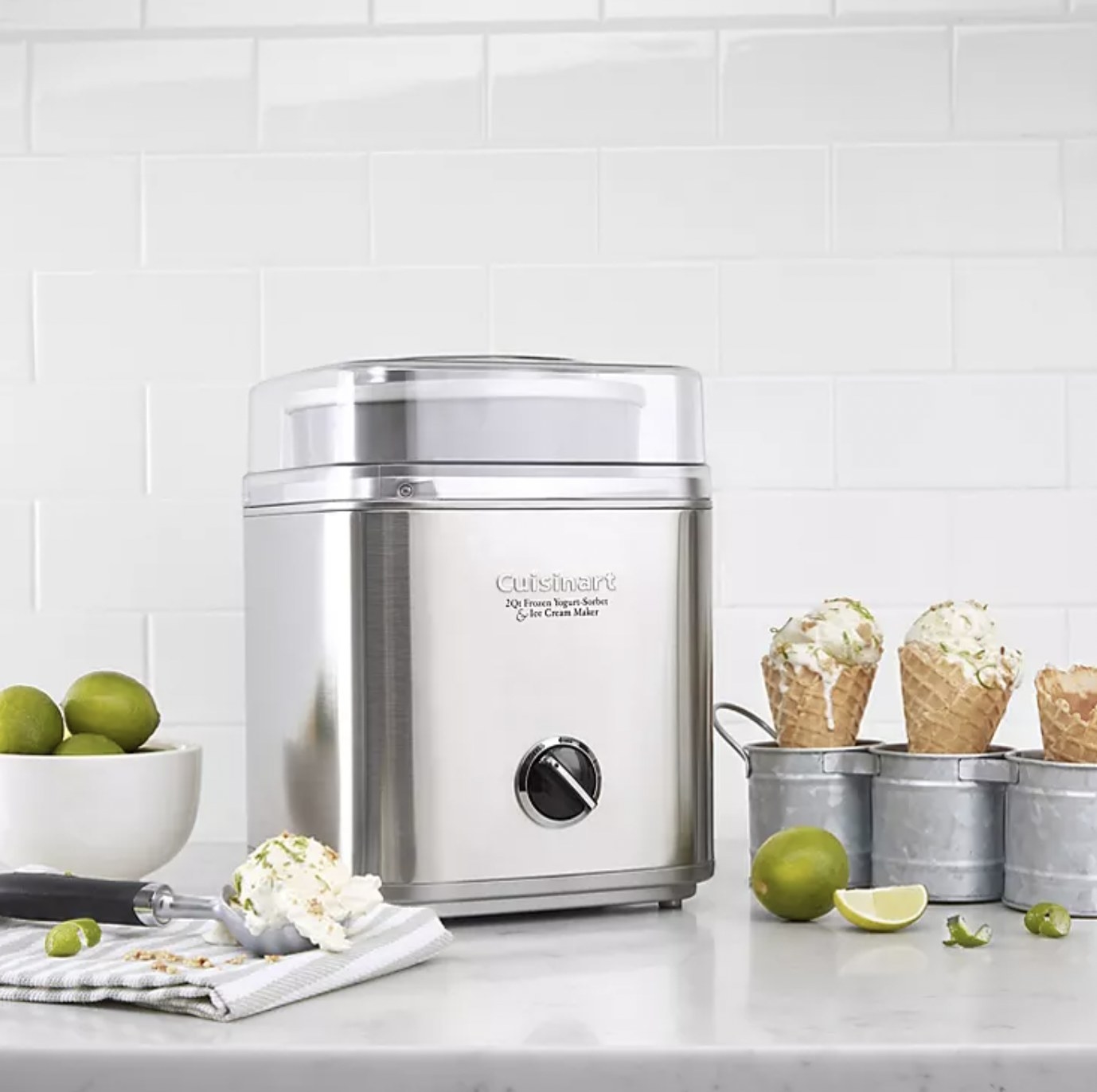 The stainless steel ice cream maker on counter with scoop of vanilla lime ice cream resting nearby and three cones with ice cream